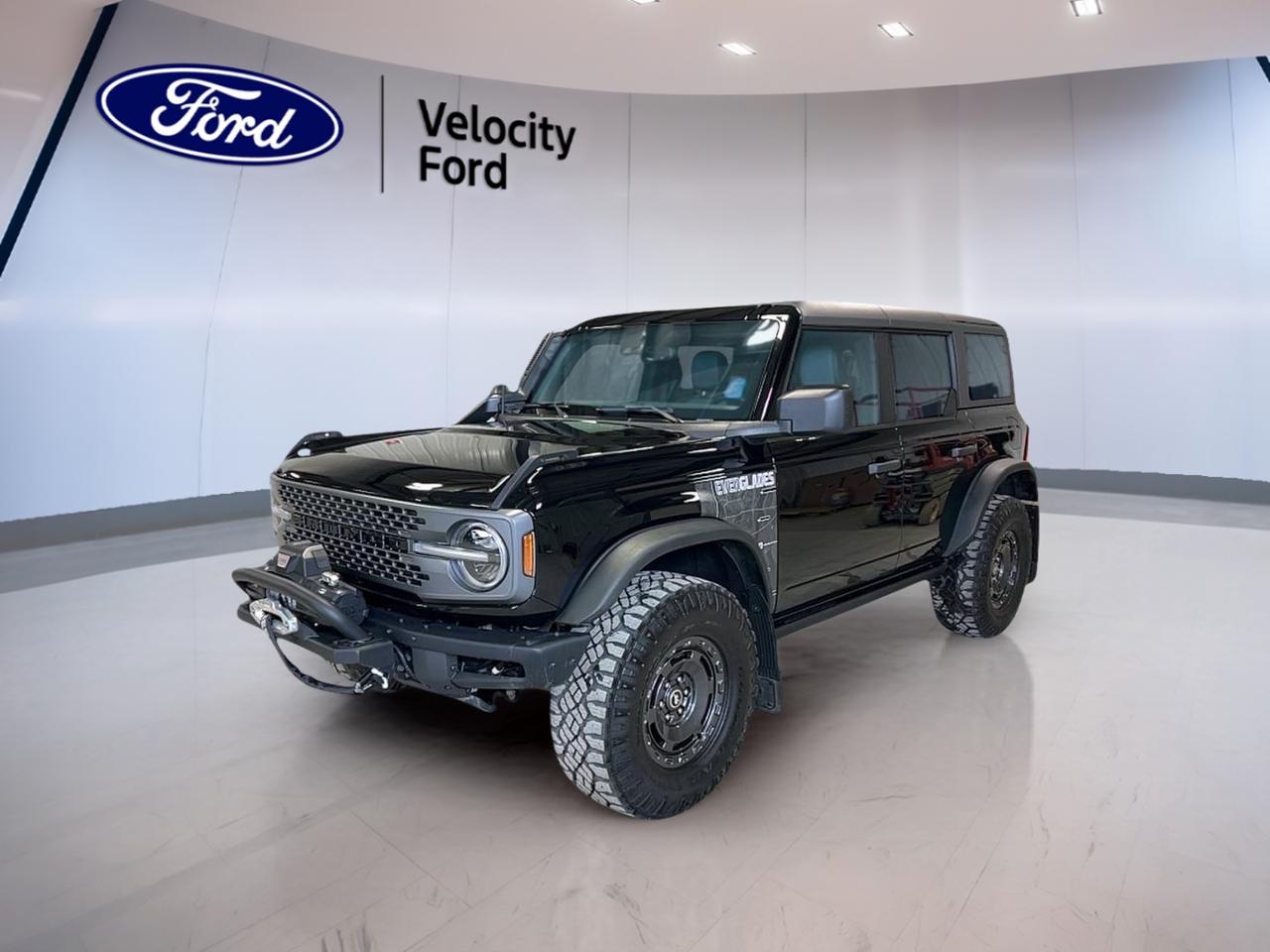 Meet the SUV 2024 Ford Bronco Everglades 4 Door Used, now available at Velocity Ford in Moose Jaw. Finished in Black outside with a Black interior, this Bronco is built for drivers who want real off-road confidence without giving up daily comfort. With 97,299 km, an automatic transmission, and a 2.3 L gas engine, its ready for the next commute, the next road trip, and the next trail.

The SUV 2024 Ford Bronco Everglades 4 Door Used brings a unique mix of rugged hardware and smart features. You get Four-Wheel Drive (4WD) for year-round traction, plus off-road tires and a limited slip differential to help you keep moving when conditions change. A convertible hardtop adds flexibility for warm-weather driving, while LED headlamps and tinted windows round out a clean, purpose-built look.

FEATURES OF THE Bronco Everglades 4 Door
»» Four-Wheel Drive for confident trail traction  
»» Convertible hardtop for open-air versatility  
»» Off-road tires for tougher terrain grip  
»» Rear tow hook for recovery support  

ADVANCED SAFETY FEATURES
»» Anti-Lock Braking System for controlled stops  
»» Stability Control helps maintain steady handling  
»» Blind Spot Monitor for safer lane changes  
»» Lane Departure Warning adds extra awareness  

PERFORMANCE AND EFFICIENCY
»» 2.3 L gas engine for daily usability  
»» Automatic transmission for smooth, easy driving  
»» Dual shift mode for manual-style control  
»» Limited slip differential improves low-grip traction  

COMFORT AND CONVENIENCE
»» Dual-zone climate control for balanced comfort  
»» Heated front seats for cold mornings  
»» Remote starter helps warm up quickly  
»» Power windows and power steering ease  

TECHNONOLGY AND CONNECTIVITY
»» Navigation System for clear route guidance  
»» Bluetooth integration for hands-free calling  
»» WiFi hotspot helps keep devices connected  
»» Steering wheel audio controls reduce distraction  

CARGO SPACE
»» Rear trunk access for easy loading  
»» Spare tire onboard for added reassurance  
»» Four-door layout improves daily practicality  
»» Convertible hardtop supports larger gear loading  

WHAT OTHER OWNERS LIKE
»» Confident 4WD capability in harsh weather  
»» Open-air feel with convertible hardtop  
»» Helpful driver aids like blind spot monitoring  
»» Easy connectivity with Bluetooth and WiFi  

This SUV 2024 Ford Bronco Everglades 4 Door Used is a great fit if you want a capable Ford SUV that still feels simple to live with. Visit Velocity Ford in Moose Jaw to see it in person and take it for a drive.

This 2024 Ford Bronco Everglades 4 Doors VIN is: 1FMEE4HH2RLA01909.