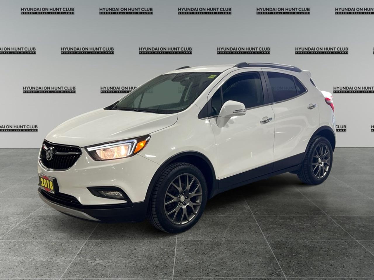 The 2018 Buick Encore Sport Touring in white is a dynamic SUV designed for those who appreciate performance and style. Its forward-wheel drive and smooth automatic transmission promise an engaging driving experience whether youre navigating city streets or country roads. The Sport Touring FWD trim is equipped with the SPORT TOURING PREFERRED EQUIPMENT GROUP, adding to its appeal. On the exterior, this white Buick Encore stands out with its modern alloy wheels and sleek lines. Inside, youll find a well-appointed cabin featuring leather steering wheel accents and heated mirrors for added comfort. The Encores versatility is matched by practical features like power seats, power windows, and a backup camera to enhance everyday convenience. Stay connected on the go with the intuitive technology suite, including a Bluetooth connection, satellite radio, smart device integration, and a Wi-Fi hotspot. Safety features such as a backup camera offer peace of mind, while remote start and keyless entry add a layer of modern ease to your daily routine. The 2018 Buick Encore Sport Touring is perfect for those who value technology and convenience without sacrificing style. Whether youre a busy professional or a growing family, this vehicle is sure to meet your needs. Contact Hyundai On Hunt Club today to schedule a test drive and explore more about how this exceptional SUV can be part of your journey.