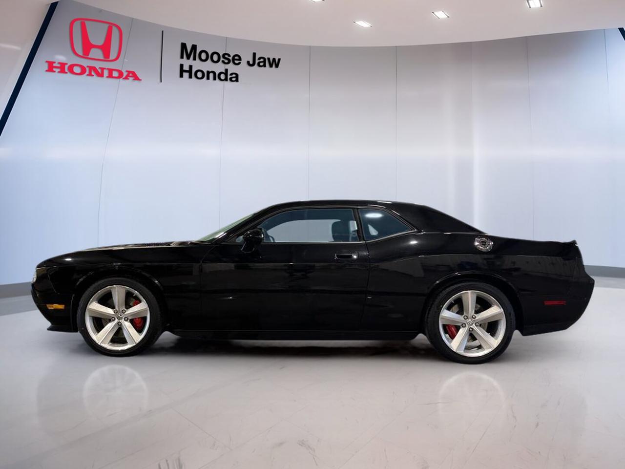 CARFAX Canada reports no accident.

Turn heads in this 2010 Dodge Challenger Srt8, now offered by Moose Jaw Honda in Moose Jaw. With just 13,254 km, a bold Black exterior, rear-wheel drive, and a 6.1L HEMI V8 engine, this coupe brings true muscle car character. The 2010 Dodge Challenger Srt8 blends classic Dodge style with modern power.

Built for drivers who want excitement, this 2010 Dodge Challenger Srt8 delivers strong V8 performance through a 5-speed automatic transmission. Its wide stance, confident road presence, and low kilometre reading make it a rare used performance coupe. This is a serious Dodge for collectors and enthusiasts alike.

FEATURES OF THE Challenger Srt8
»» 6.1L HEMI V8 delivers strong power
»» Five-speed automatic handles shifts with ease
»» Rear-wheel drive supports classic muscle feel
»» Low 13,254 km adds rare appeal

ADVANCED SAFETY FEATURES
»» Four-wheel disc brakes support controlled stopping
»» Electronic stability control helps maintain balance
»» Traction control aids grip on takeoff
»» Advanced front airbags enhance occupant protection

PERFORMANCE AND EFFICIENCY
»» HEMI V8 provides thrilling acceleration response
»» Rear-wheel drive delivers authentic coupe dynamics
»» Automatic transmission offers smooth power delivery
»» Performance-tuned chassis supports confident cornering

COMFORT AND CONVENIENCE
»» Two-door coupe design allows easy front access
»» Spacious cabin suits relaxed highway cruising
»» Air conditioning helps keep cabin comfortable
»» Cruise control supports easy long drives

TECHNOLOGY AND CONNECTIVITY
»» Clear driver gauges show vital information
»» Audio system supports daily entertainment needs
»» Steering wheel controls improve driver ease
»» Simple centre layout keeps functions accessible

CARGO SPACE
»» Trunk space handles weekend travel bags
»» Wide opening helps loading larger items
»» Rear seatback access adds carrying flexibility
»» Coupe design still offers useful storage

AWARDS & RECOGNITIONS
»» Best Resale Value Sports Car, Kelley Blue Book, 2010

WHAT OTHER OWNERS LIKE
»» Strong V8 sound and power delivery
»» Classic muscle styling with modern comfort
»» Stable highway ride and road presence
»» Low production feel and collector appeal

For drivers who appreciate real Dodge muscle, this coupe stands out with proven HEMI performance and very low kilometres. The Black finish adds a clean, aggressive look, while the automatic transmission makes this performance car easy to enjoy in town or on the open highway.

This used 2010 Dodge Challenger Srt8 is a smart choice for anyone seeking a memorable weekend car or a standout addition to a garage. It offers the sound, feel, and presence expected from a true Dodge performance coupe, backed by a clean CARFAX Canada report and available now at Moose Jaw Honda.

This 2010 Dodge Challenger Srt8s VIN is: 2B3CJ7DW0AH129422.