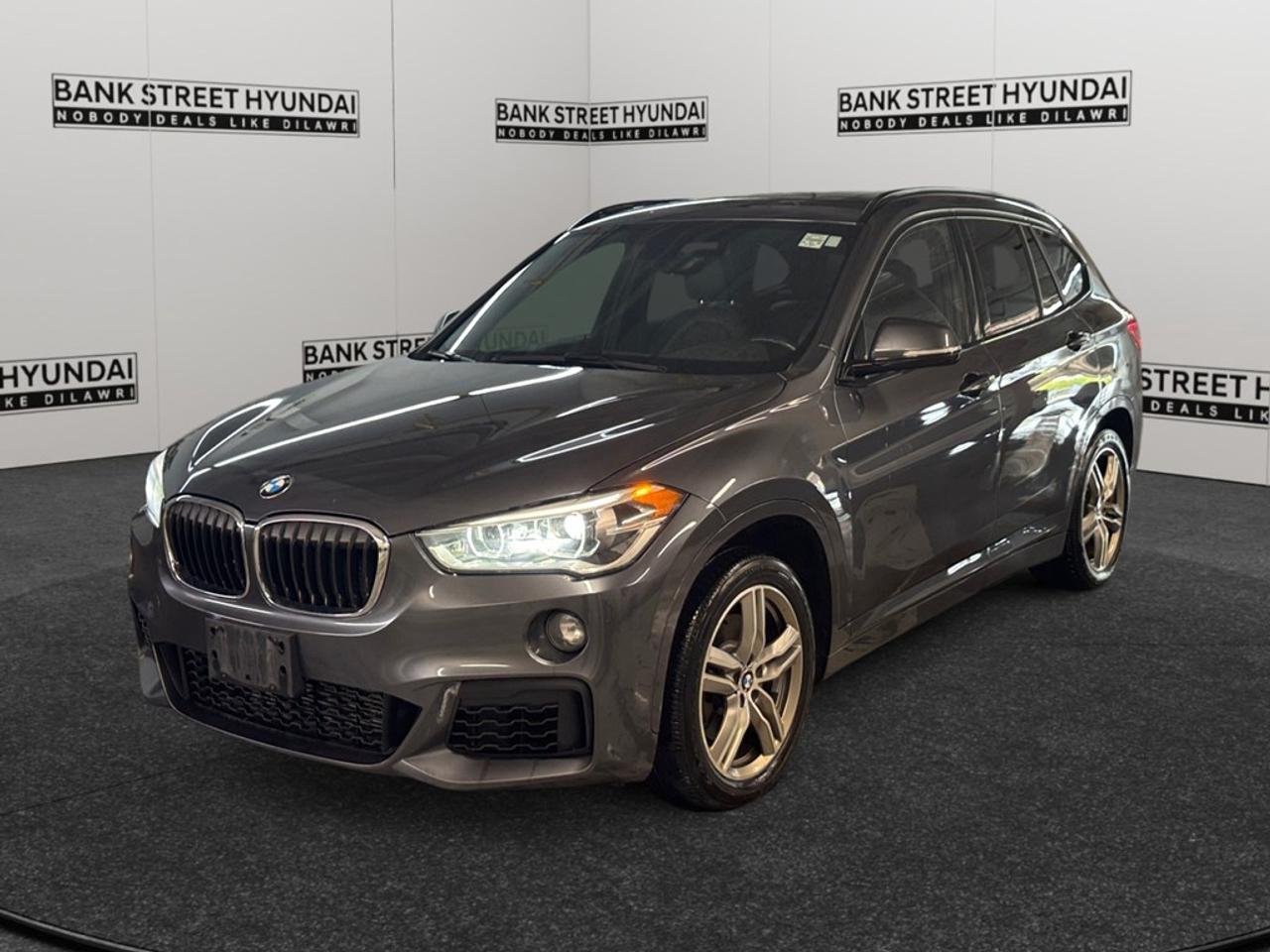 Experience the thrill of driving with this suave 2018 BMW X1 xDrive28i Sports Activity Vehicle, featuring a glossy black exterior and advanced all-wheel drive system. This exquisite SUV promises responsive handling, perfectly blending luxury with performance to make every journey an occasion to Remember. Its sophisticated exterior is complemented by alloy wheels that provide both style and functionality. Slide inside to a meticulously designed cabin, featuring a leather steering wheel and leatherette door trim inserts for an added touch of luxury. The leather/metal-look gear shifter contributes to the overall elegant interior atmosphere. Technology meets comfort seamlessly with features such as Bluetooth connection, smart device integration, and a convenient backup camera ensuring connectivity and safety on the go. Youll appreciate the heated mirrors and front seats, perfect for those chilly days, while brake assist and parking sensors add an extra layer of security. Additionally, keyless entry and cruise control offer ease and convenience for your driving experience. This BMW X1 is ideal for those who seek a blend of luxury and practicality in their SUV. Perfect for families or individuals with an active lifestyle, its designed to keep you comfortable while driving in style. Contact Bank Street Hyundai to arrange a test drive and learn more about this impressive vehicle today!